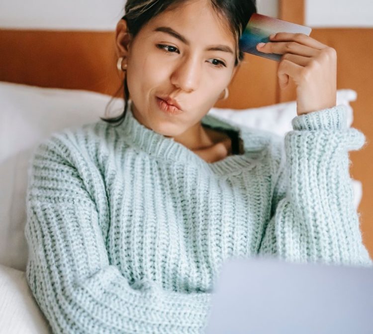 Source: https://www.pexels.com/photo/pensive-ethnic-shopper-with-debit-card-and-laptop-on-bed-6347709/