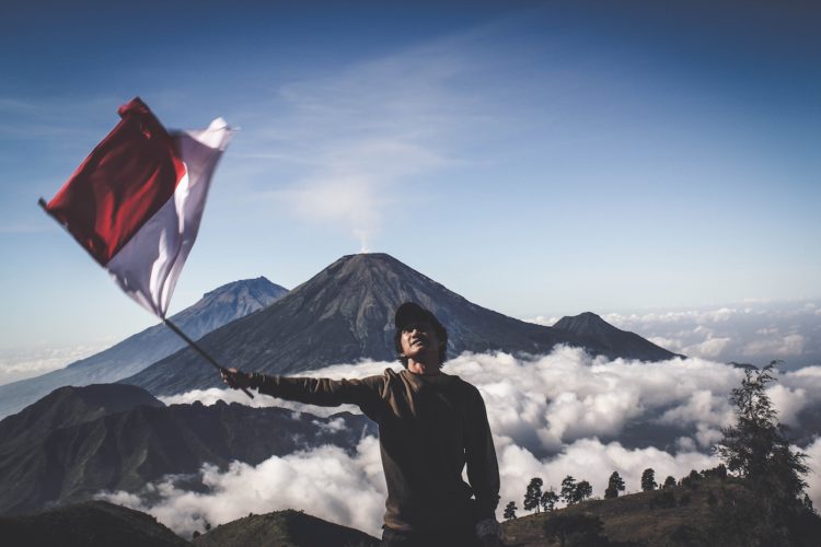 Photo by Dio Hasbi Saniskoro: https://www.pexels.com/photo/man-wearing-black-crew-neck-sweater-holding-white-and-red-flag-standing-near-mountain-under-blue-and-white-sky-1009949/